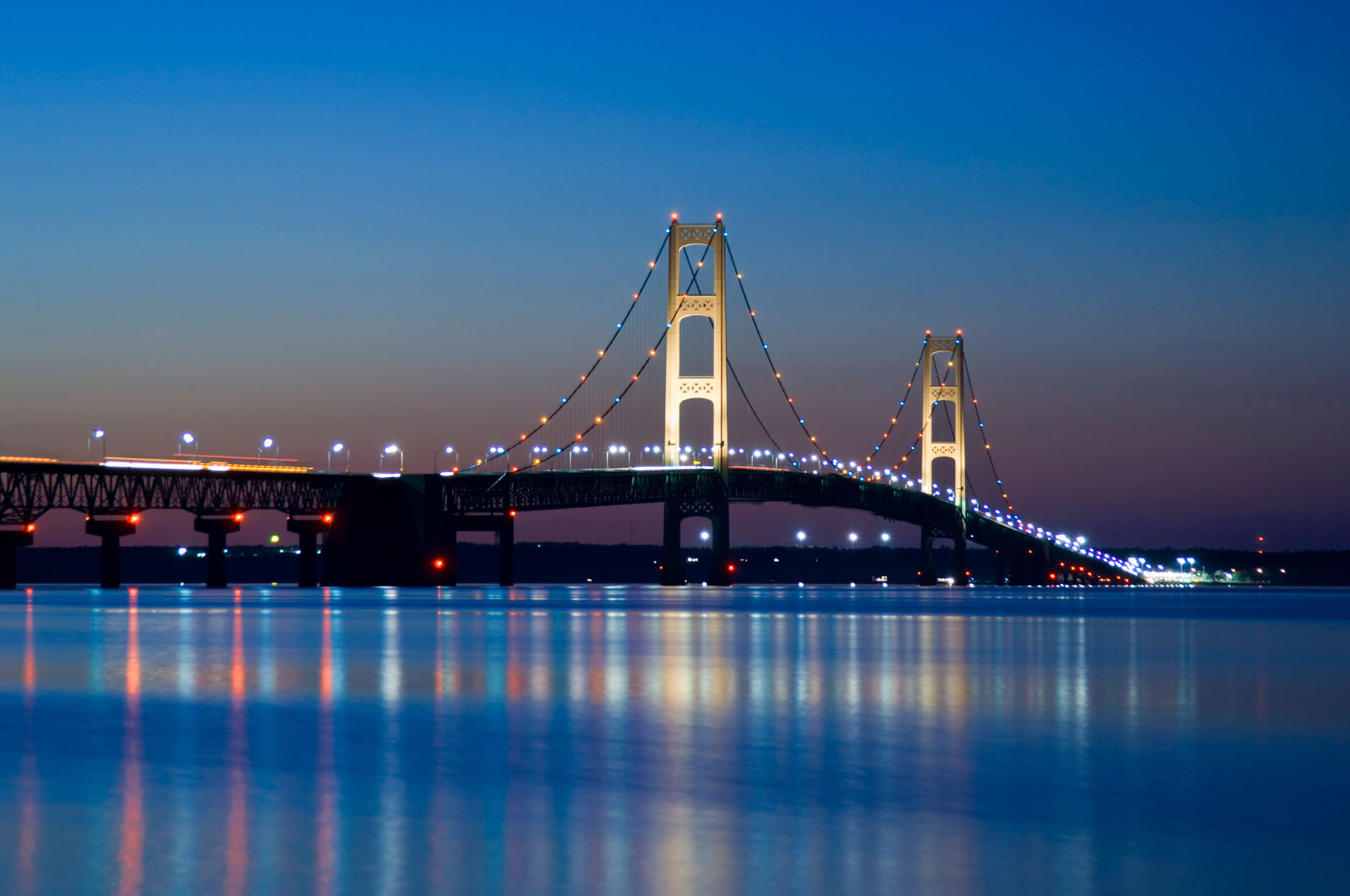The Mackinac Bridge lit at dusk, reflected in the Straits
